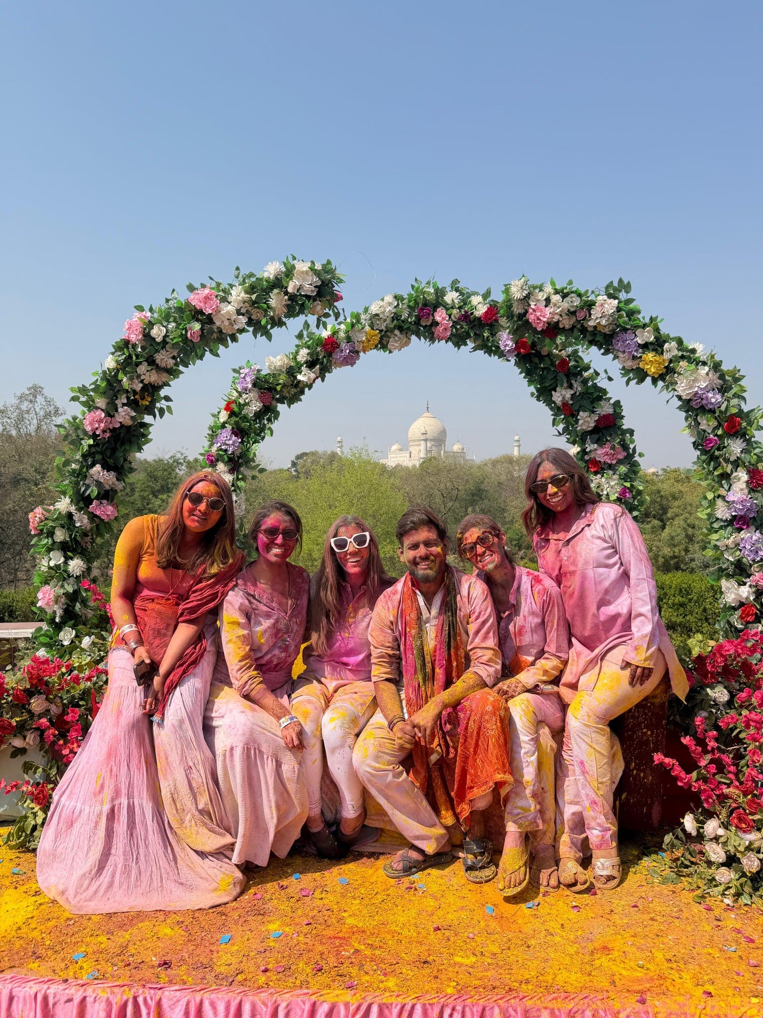 Travellers covered in Holi colours under a floral arch with the Taj Mahal behind them in Agra